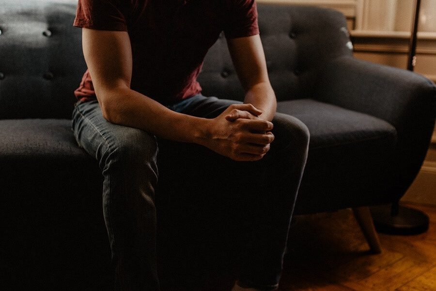En mann som søker avhengighetsterapi, sitter på en sofa med hendene foldet